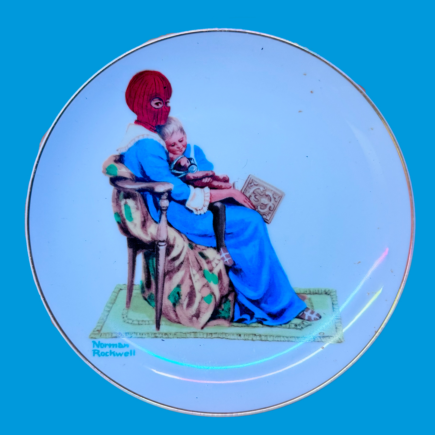 Decorative plate with a scene of a woman in a blue dress and  painted to be wearing a red balaclava sitting on a chair. On a blue background