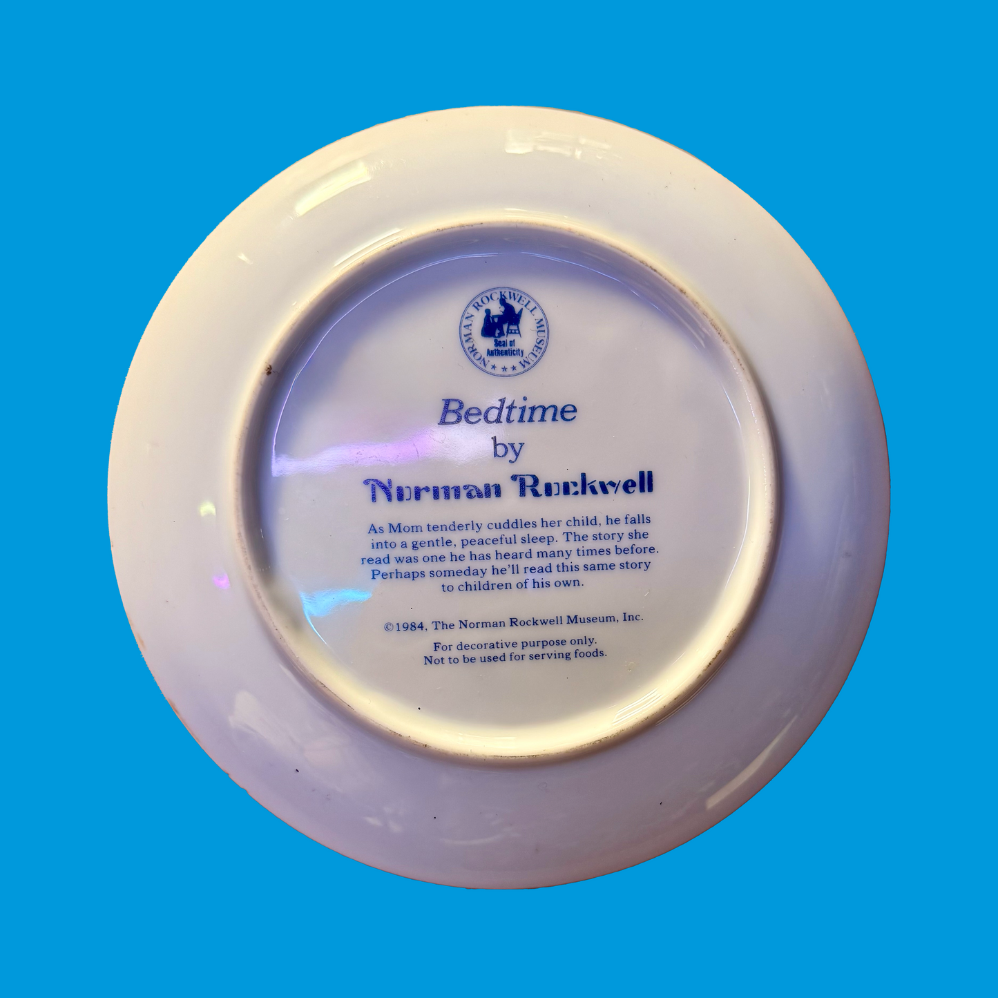 Decorative plate back with 'Bedtime' by Norman Rockwell written on it, on a blue background